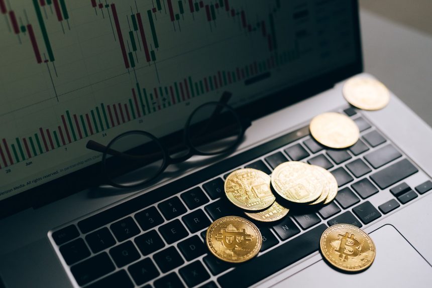 Dizüstü bilgisayar klavyesi üzerinde Bitcoin sikkeleri, ekranda mum grafiği