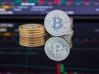 Altın ve gümüş renkli Bitcoin sikkeleri, arkada bulanık işlem ekranı